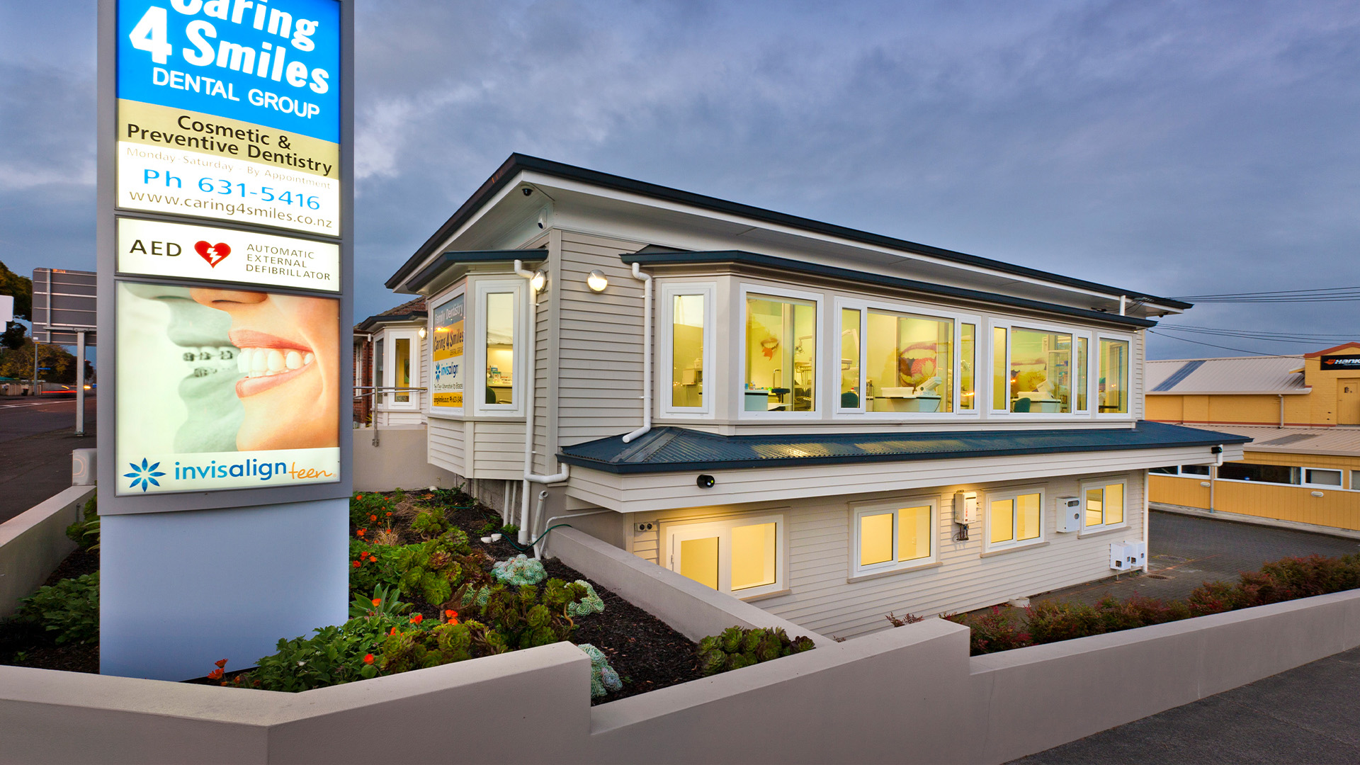 The Caring 4 Smiles dental practice and street sign on Manukau Road, Epsom, at dusk